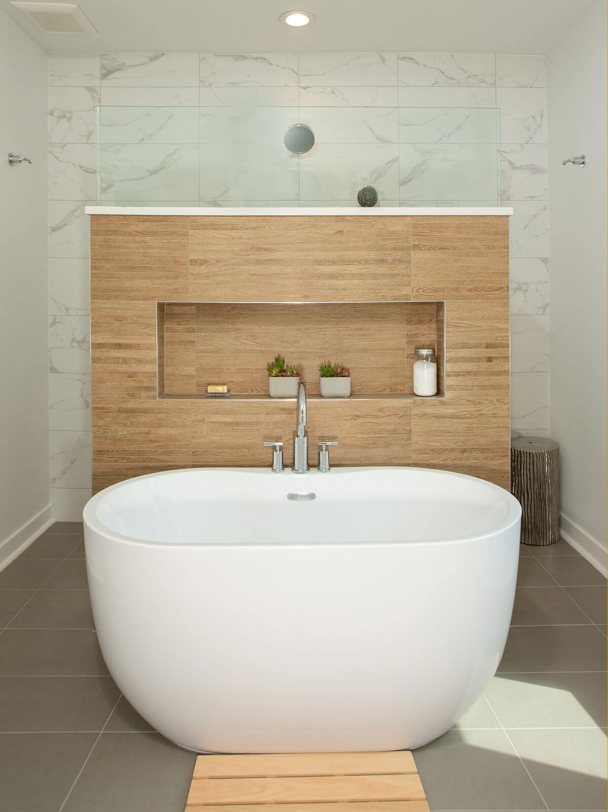 Modern freestanding bathtub with wood-paneled wall and recessed shelving.