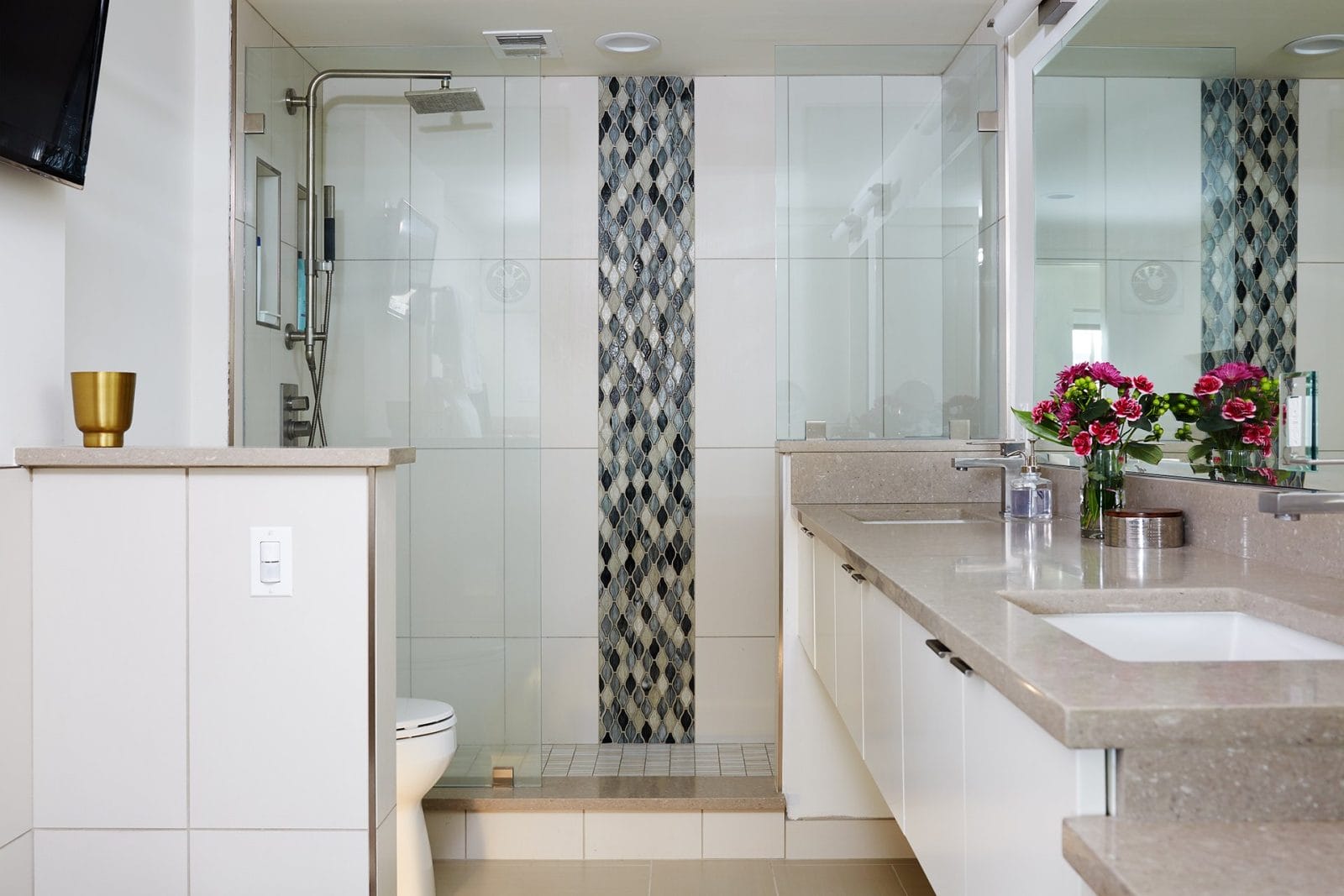 Frameless shower enclosure with vertical accent tile in a modern bathroom featuring light countertops and a spacious vanity.